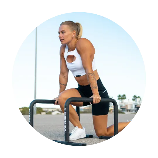Woman performing a calisthenics exercise using parallettes, wearing a white workout top and black shorts, with a focused expression.