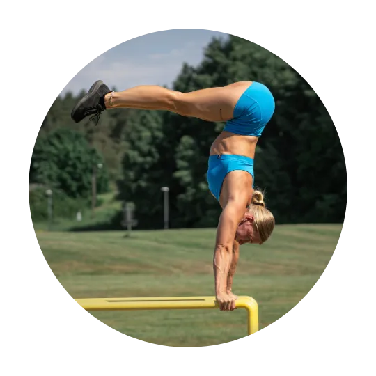 Woman performing an advanced handstand on parallel bars outdoors, wearing a blue workout set.