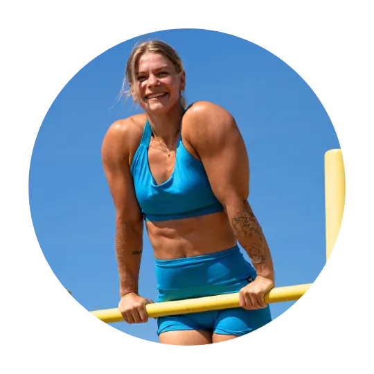 Woman smiling and demonstrating strength on parallel bars, wearing a blue workout set, with the clear blue sky in the background.