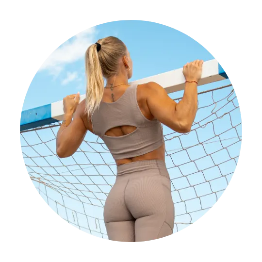 Woman performing a pull-up on a horizontal bar, wearing a beige workout set, with a clear blue sky in the background.
